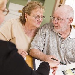 Elderly couple reviews documents with a professional at a table.