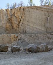 Steinbruch mit steilen Wänden, groben Felsen am Boden und einem klaren Himmel darüber.