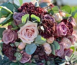 Ramo de flores con rosas rosadas y hortensias moradas, rodeado de hojas verdes.
