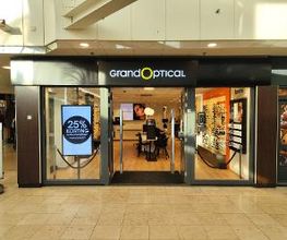 Winkeluitgang van Grand Optical met reclamebord en briluitstalling aan de rechterkant.