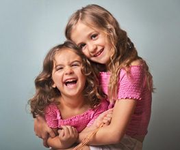 Dos niñas sonriendo y abrazándose, ambas vestidas con camisetas rosas.