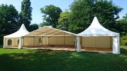 Großes Festzelt mit weißen Kuppeln auf grüner Wiese vor Bäumen an einem sonnigen Tag.