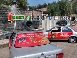 Dos autos con altavoces anunciando un evento cultural en una calle residencial.