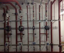 Rote Rohre und Ventile an einer Wand, Teil eines Heizungs- oder Wasserleitungssystems.