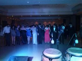 Grupo de personas bailando en fila en un salón, con micrófonos y tambores al frente.