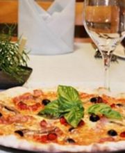 Pizza auf gedecktem Tisch mit Weingläsern und Besteck, dekoriert mit Basilikumblättern.