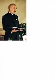 Ein Mann in dunkler religiöser Kleidung hält ein aufgeschlagenes Buch in den Händen.