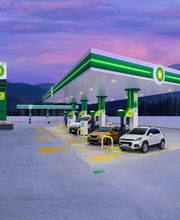 Estación de servicio iluminada al atardecer con coches cargando bajo un cielo púrpura.