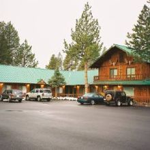 Rustic lodge with green roofs, surrounded by trees and cars parked in front.