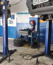 Oficina mecânica com dois carros levantados em elevadores hidráulicos. Ferramentas ao fundo.