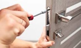 Personne réparant une serrure de porte avec un tournevis.
