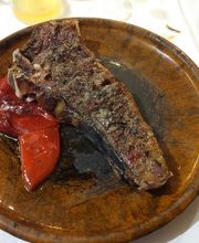 Asado en plato de cerámica con pimientos rojos asados. Cuchillo a la derecha.