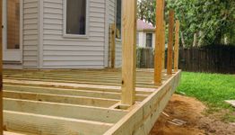Wooden deck frame under construction attached to a house, surrounded by a grassy yard.