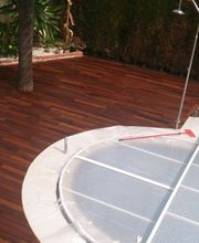 Piscina con cubierta y terraza de madera, rodeada de vegetación y ducha exterior.
