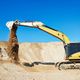 Excavator moving dirt in a sunny construction site against a clear blue sky.