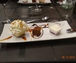 Postre en plato rectangular con mousse, trufa de chocolate, crema y cucharas sobre mesa oscura.