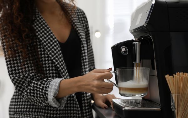 Mitarbeiterin bereitet sich an einer modernen Kaffeemaschine einen Kaffee zu.