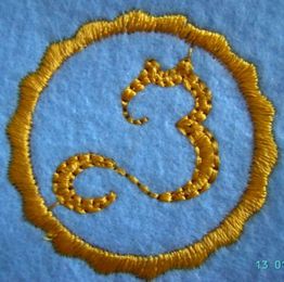 Gestickte gelbe Katze im Kreis auf blauem Stoff.