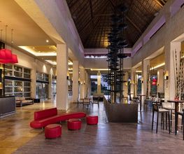 Vestíbulo moderno con techo alto, muebles rojos y bar iluminado.