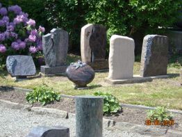 Gräber in einem Friedhof mit bunten Grabsteinen, umgeben von Blumen und grünem Garten.