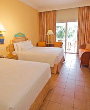 Habitación de hotel con dos camas, escritorio, balcón y decoración en tonos cálidos.