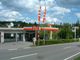 Tankstelle mit AVIA-Logo, rot-weißen Fahnen, umgeben von Bäumen und blauen Himmel im Hintergrund.