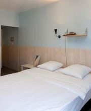 Helles Schlafzimmer mit Doppelbett, weißer Kommode, zwei Stühlen und einem kleinen Tisch.