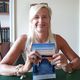 Una donna sorride, seduta a un tavolo, e tiene un libro intitolato "Ipnosi e Mindfulness".