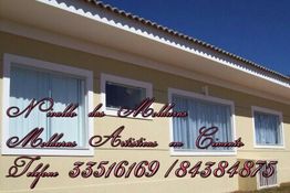 Fachada de prédio com janelas brancas e texto em letras cursivas sobre molduras artísticas.