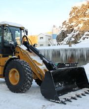 Radlader im verschneiten Steinbruch mit Felswand und vereisten Stalaktiten im Hintergrund.