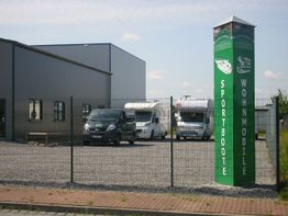 Gewerbegebäude mit Wohnmobilen und Fahrzeugen, grüner Werbeschild für Sportboote.