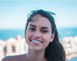 Smiling woman with sunglasses on head, with city and blue sky in the background.