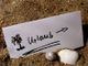 Notiz im Sand mit Palmenzeichnung und "Urlaub"-Schrift. Muscheln daneben.