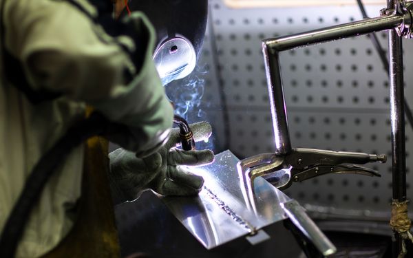 Ein Schweißer bei der Arbeit. Er verschweißt eine Schweißnaht an einem metallischem Bauteil.