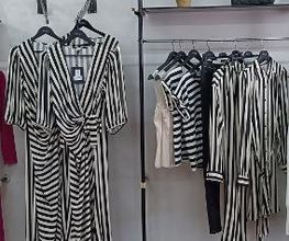 Vestidos y camisas de rayas blancas y negras colgados en un perchero en una tienda.