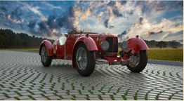 Roter Oldtimer auf gepflasterter Straße vor bewölktem Himmel mit Sonnenuntergangslicht.
