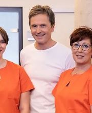 Fünf Personen posieren lächelnd, vier in orangefarbener Kleidung, eine in einem weißen T-Shirt.