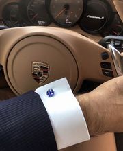 Mann mit Anzug hält Porsche-Lenkrad. Armaturbrett im Hintergrund, Manschettenknopf sichtbar.