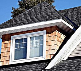 A house with a gable roof, shingle siding, and a double-hung window under a clear blue sky.