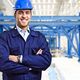 Smiling engineer in blue helmet and uniform stands inside a modern industrial facility.