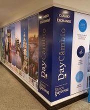 Fachada de casa de câmbio em shopping com fotos de pontos turísticos e placas informativas.