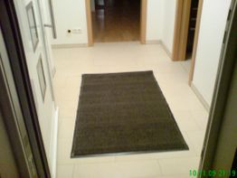 Flur mit beigem Fliesenboden und dunklem Teppichläufer, Holztür im Hintergrund.