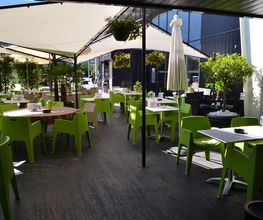 Außenterrasse mit grünen Stühlen und Sonnenschirmen in einem modern gestalteten Café.