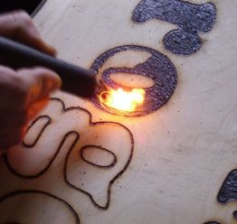 Person brennt mit Lötkolben Muster in Holzbrett.