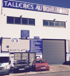 Edificio de taller mecánico con coches estacionados al frente y un cartel grande arriba.