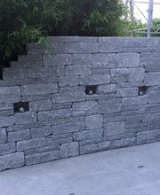 Graue Ziegelmauer mit abgestufter Kante, eingebettetem Licht, steht vor Bambus und Wand.