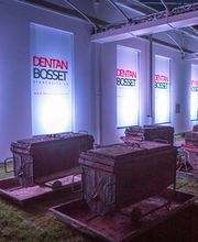 Veranstaltungsfläche bei Nacht mit beleuchteten Plakaten von Dentan Bosset und Industrie-Objekten.