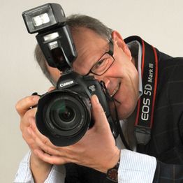 Fotograf mit Brille lächelt, während er eine Canon EOS 5D Mark III Kamera in der Hand hält.