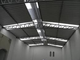 Teto metálico com estruturas de suporte em um galpão industrial, iluminado por luz natural.
