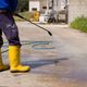 Person using a pressure washer on concrete, wearing yellow boots.